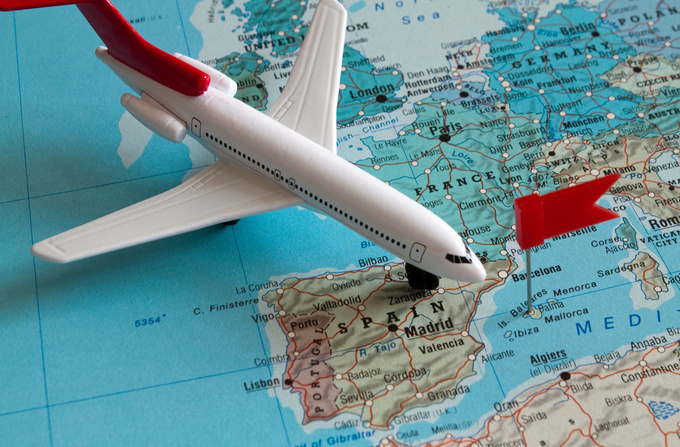 Spielzeugflugzeug mit rotem Heck auf einer Landkarte über Spanien und Portugal neben einer roten Stecknadel. Foto: Daniel Ernst/Adobe Stock